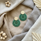 Green beaded earrings on a textured fabric surface with wooden beads and decorative leaves.