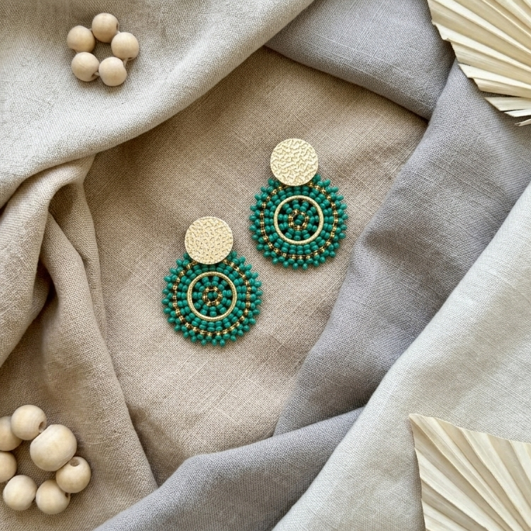 Green beaded earrings on a textured fabric surface with wooden beads and decorative leaves.