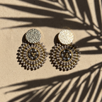 Pair of grey beaded earrings on a beige surface with palm leaf shadow
