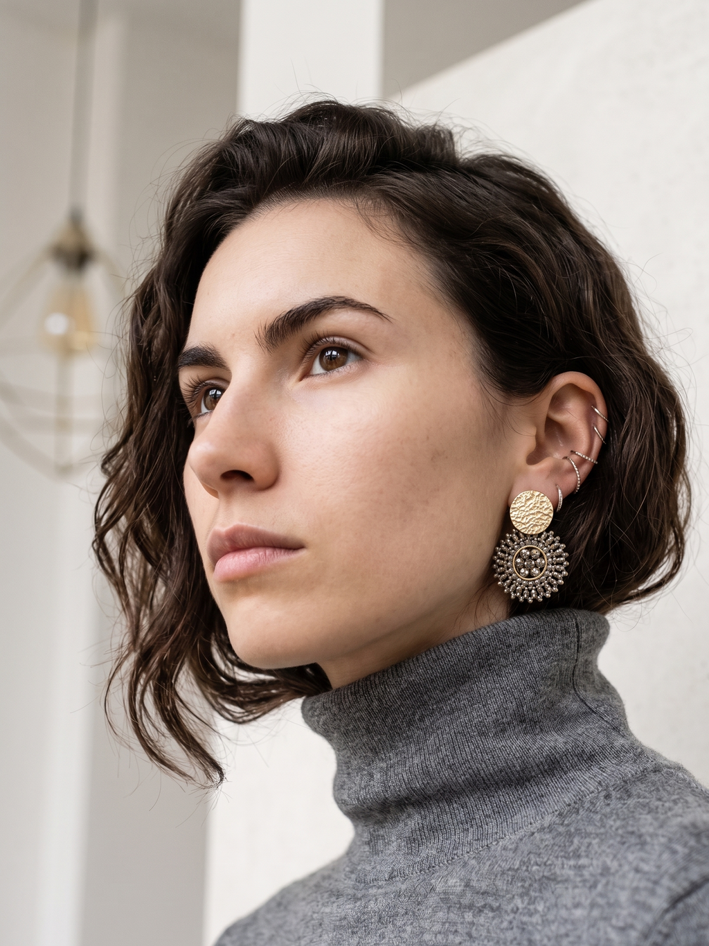 Woman wearing gold & grey earrings with a neutral background