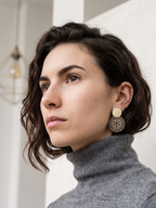 Woman wearing gold & grey earrings with a neutral background