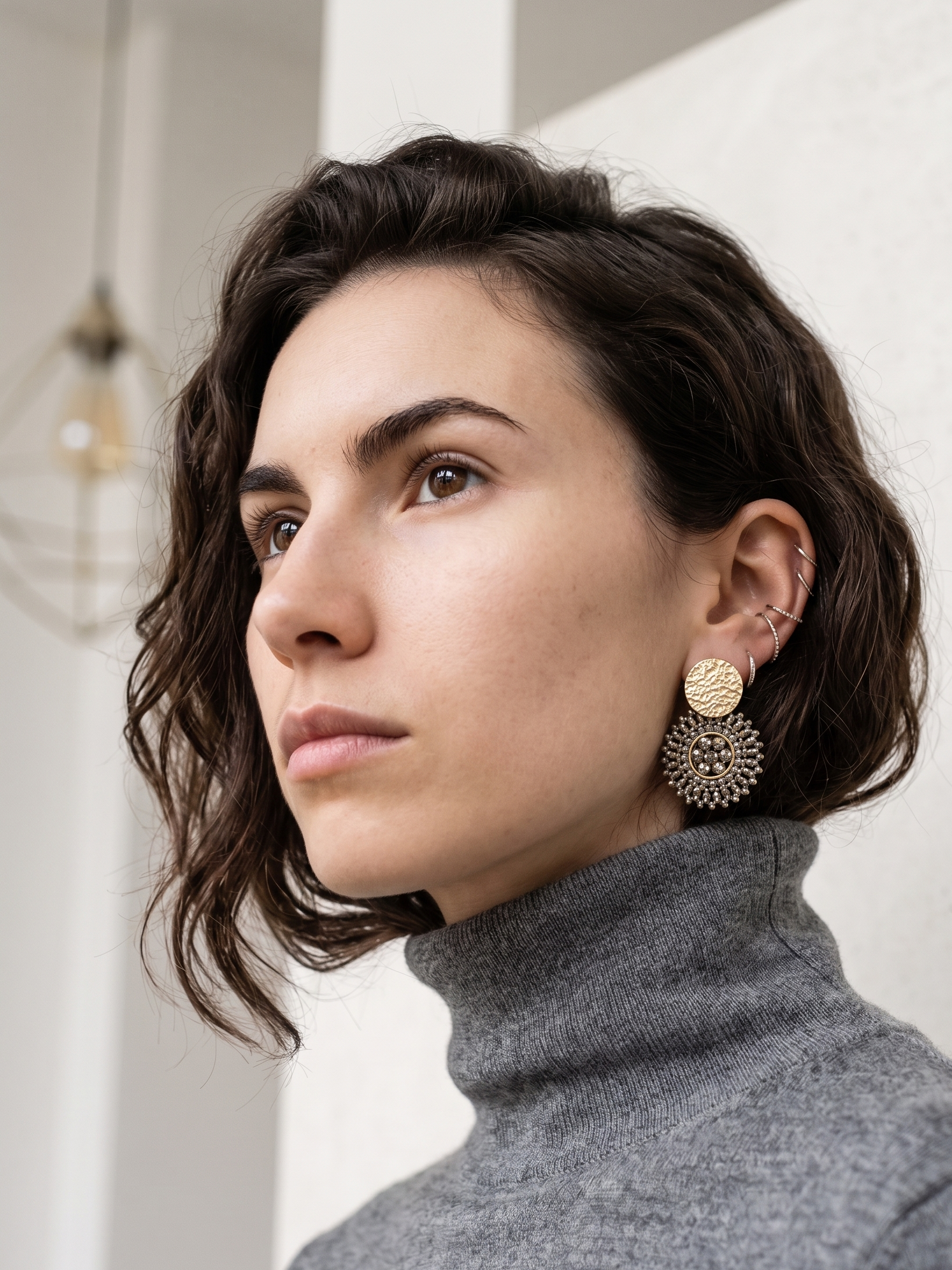 Woman wearing gold & grey earrings with a neutral background