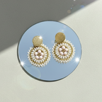 Pair of gold and pearl earrings on a round blue mirror with a soft focus background