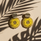 Yellow beaded earrings on a beige surface with palm leaf shadows