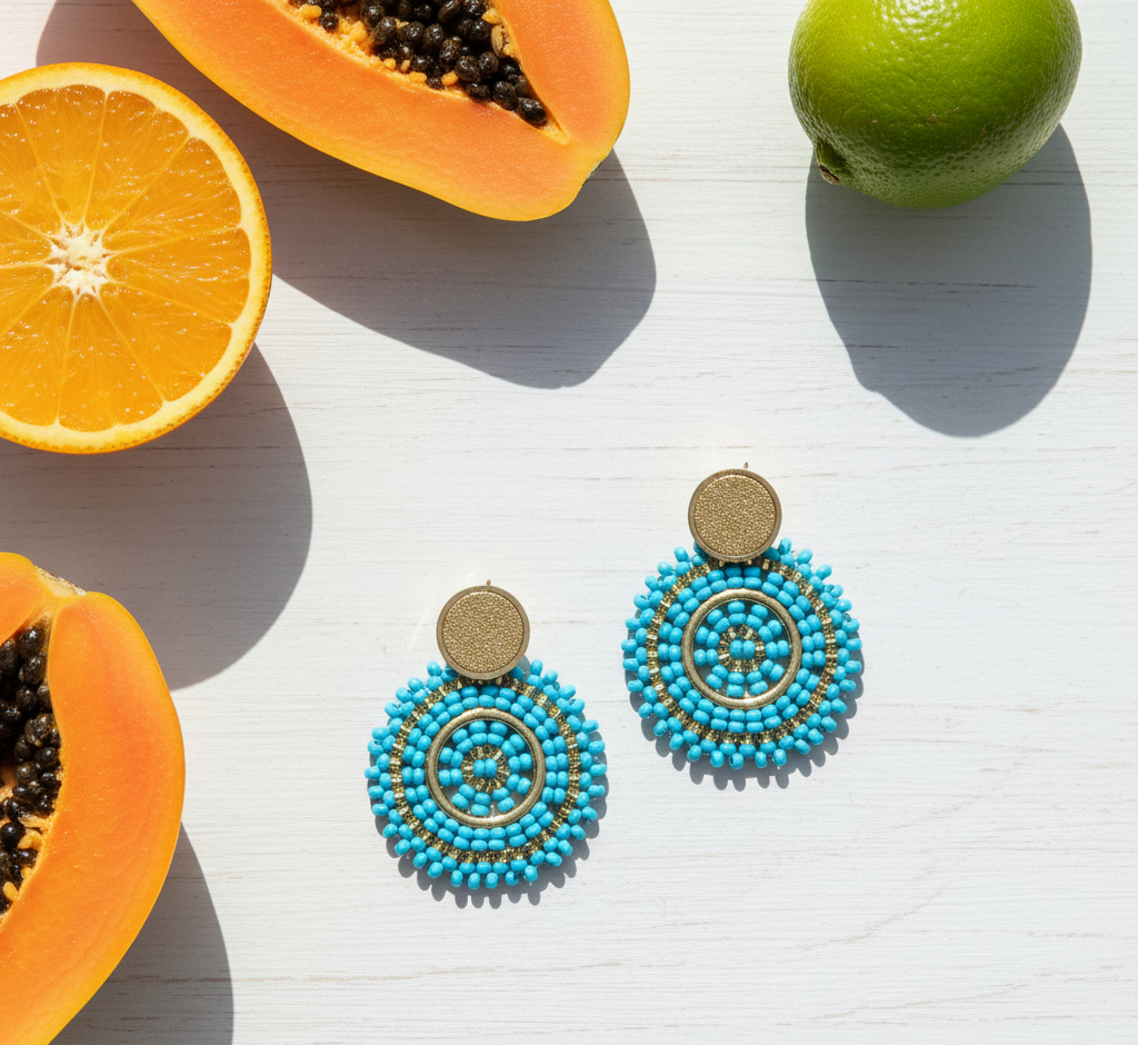 Blue beaded earrings on a white surface with papayas and a lime.