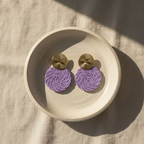 Pair of purple earrings with gold tops on a beige plate.