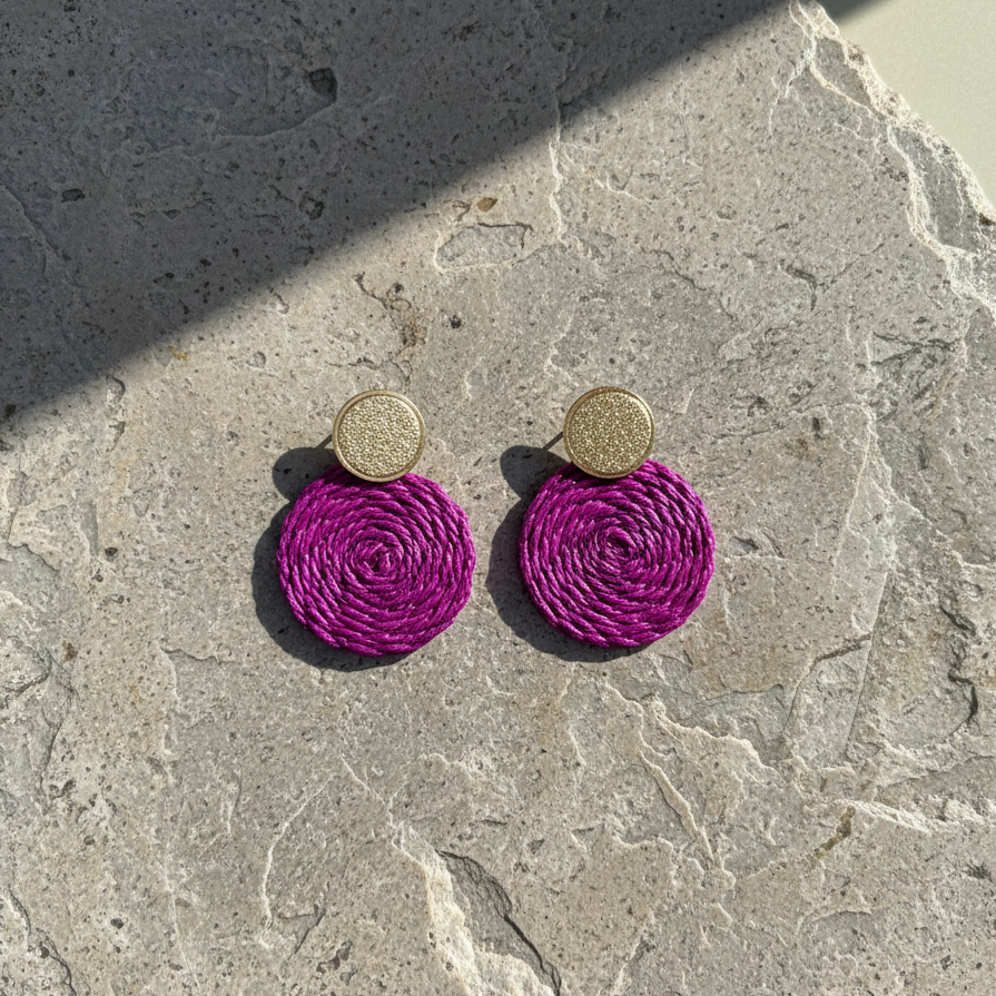 Plum circular earrings with gold tops on a stone surface