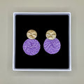 Purple earrings with gold tops in a black box on a beige background