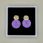 Purple earrings with gold tops in a black box on a beige background