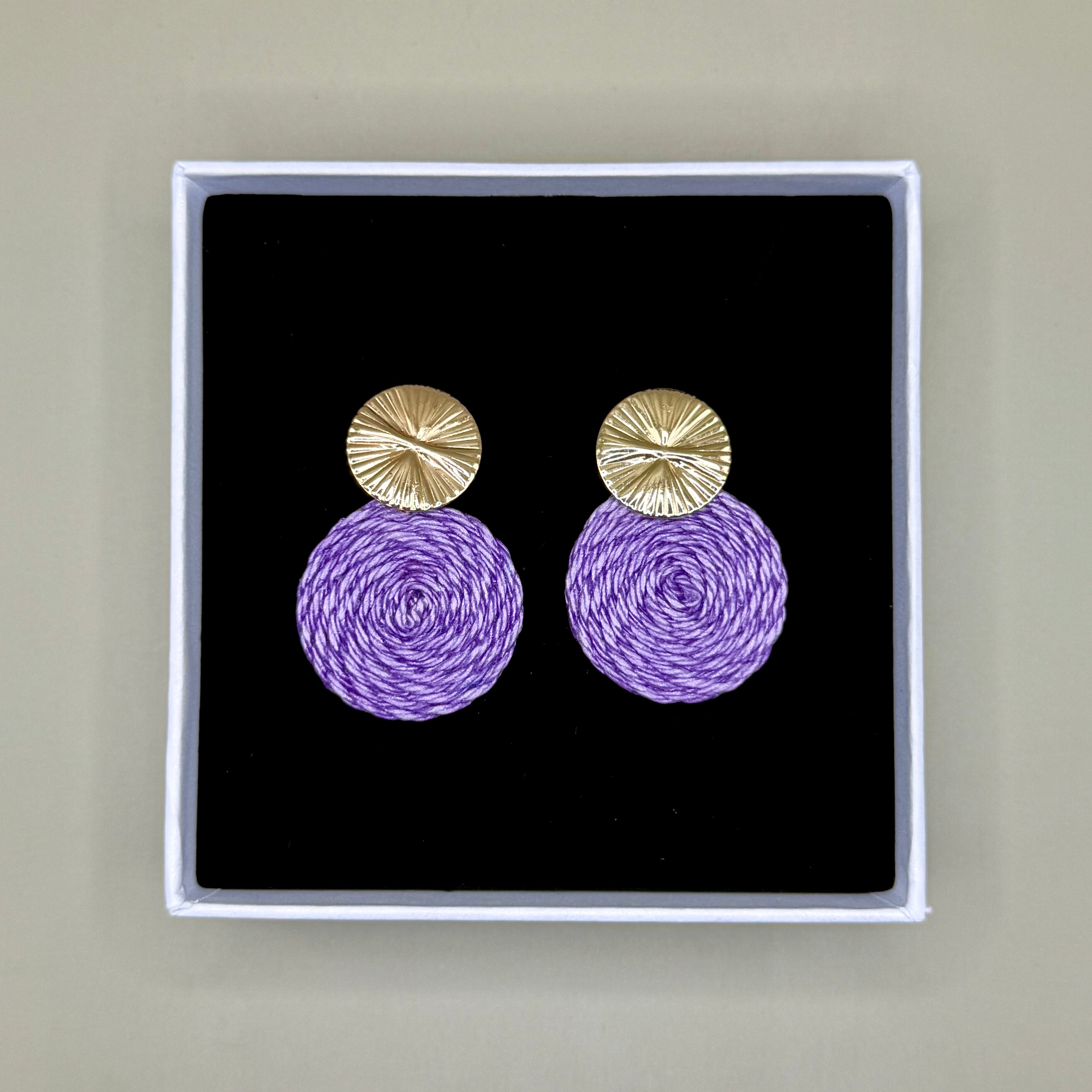 Purple earrings with gold tops in a black box on a beige background