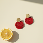Red palma earrings with gold studs on a beige background with a lemon slice.
