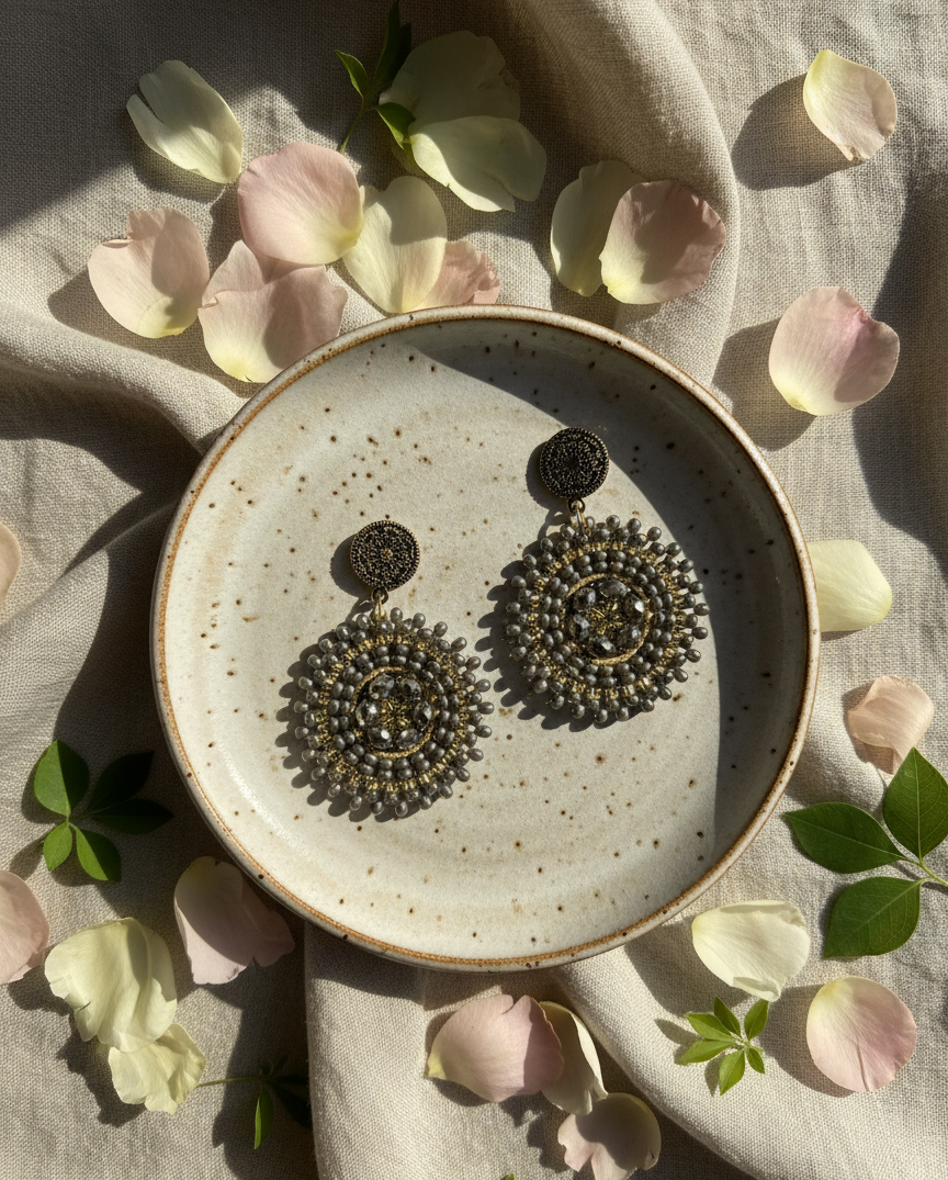 Pair of Manila small silver earrings on a speckled ceramic plate with pink petals and green leaves.